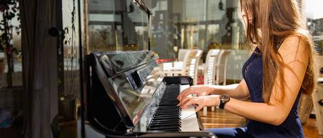 A woman playing a grand piano in a room with large windows and modern furniture.