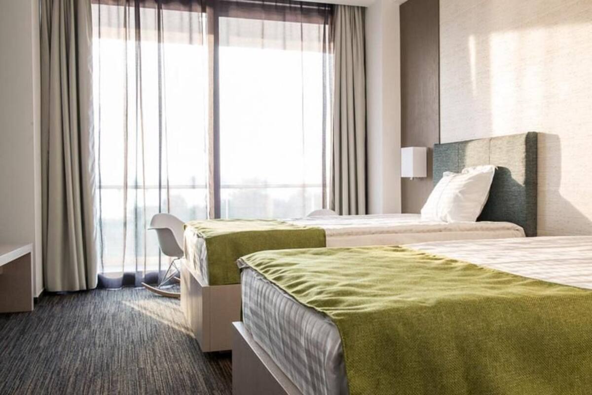 A hotel room with two beds, a desk, a chair, and a large window with curtains.