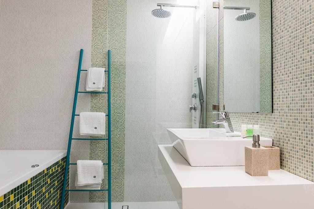 Une salle de bain moderne avec une étagère en verre où sont rangées les serviettes, un lavabo blanc avec un miroir et un espace douche.