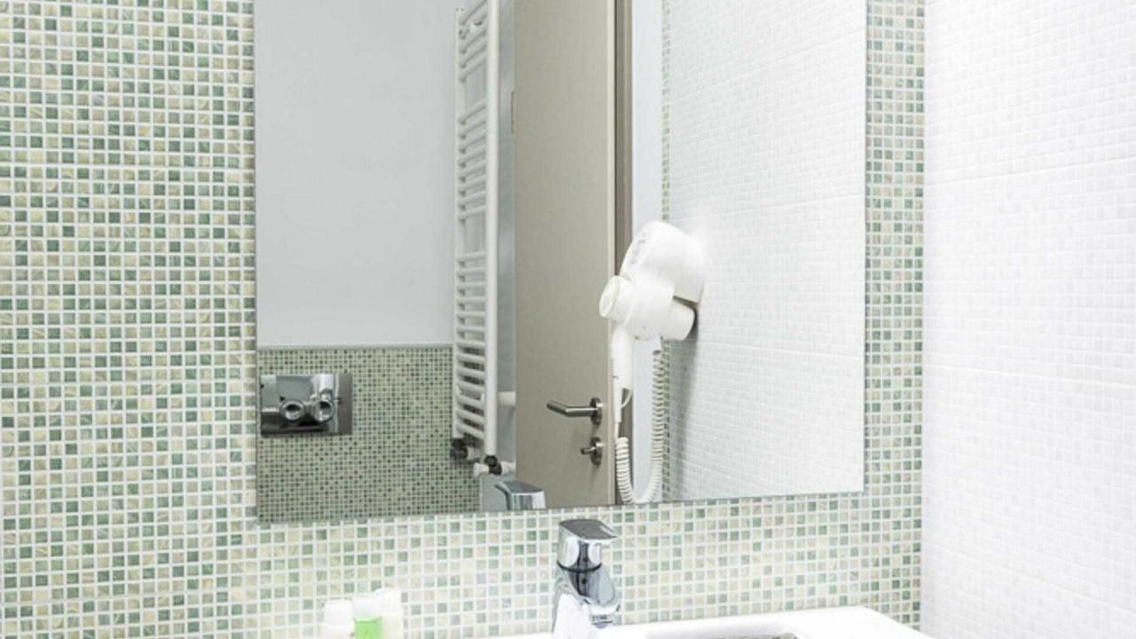 Ein Badezimmer mit gefliesten Wänden, einem Spiegel, einem Föhn und einem Waschbecken.