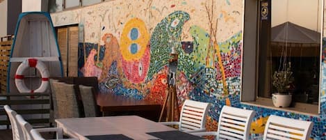An outdoor seating area with a mosaic wall, a table with chairs, and a lifebuoy.