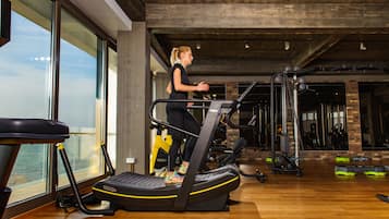 Un gimnasio con cinta de correr, equipo de ejercicio y amplias ventanas con vistas a un cuerpo de agua.