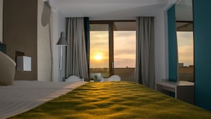 Habitación de hotel con una cama grande, un escritorio y vistas a la puesta de sol por la ventana.