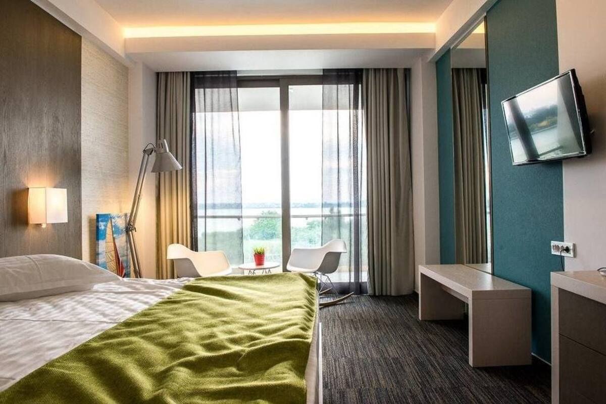 A hotel room with a bed, a desk, a chair, a TV, and a window with curtains.