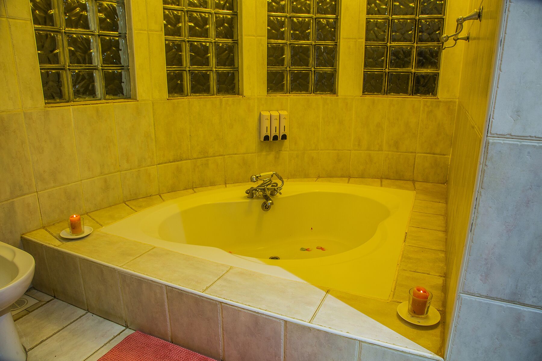 Un baño con una bañera grande, un inodoro y un lavabo. Hay dos velas en el suelo.