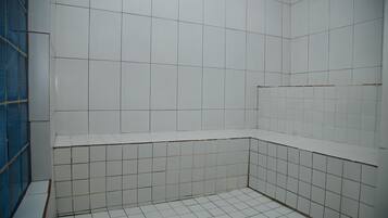 Shower area features a blue safety barrier and white tiles.