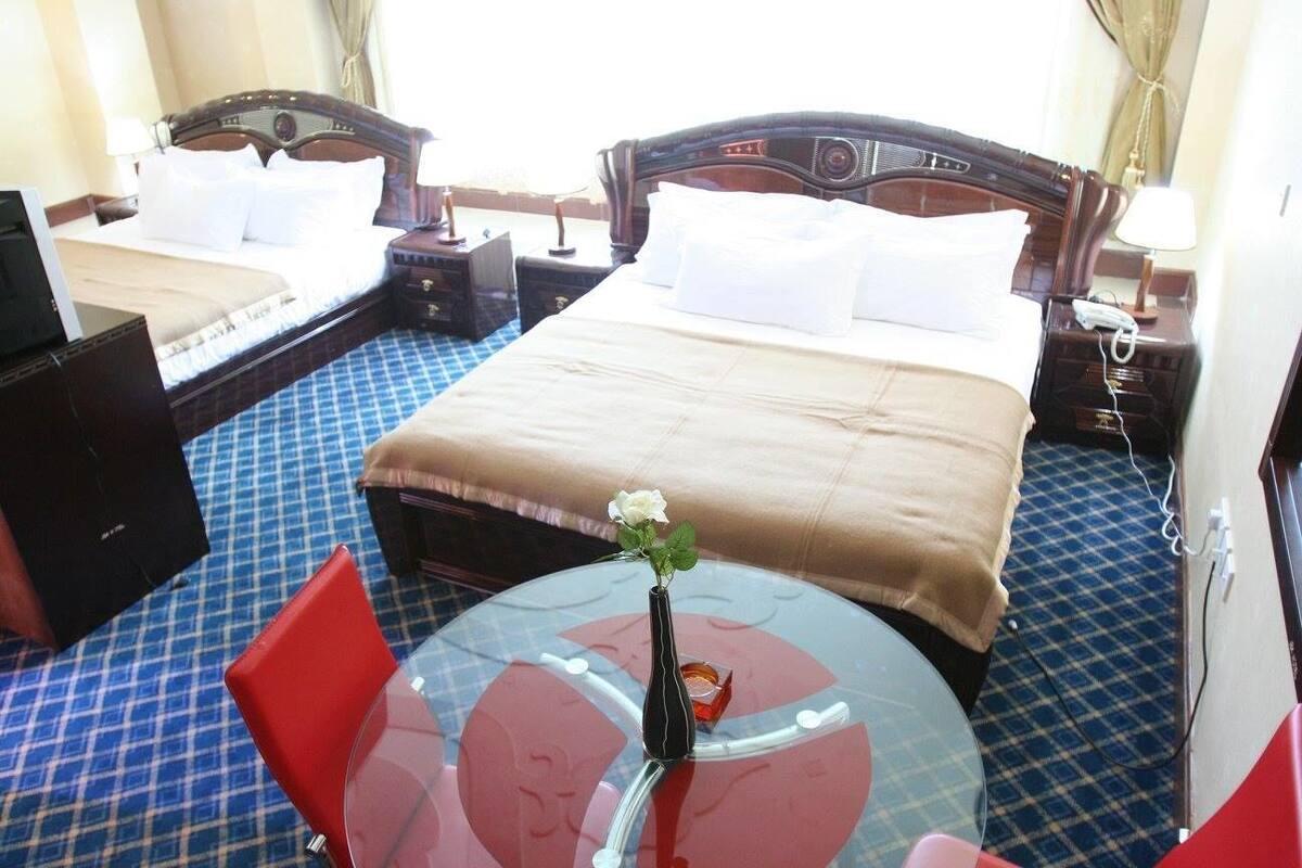 Une chambre d’hôtel avec deux lits, une table en verre ornée d’un vase et des chaises rouges.