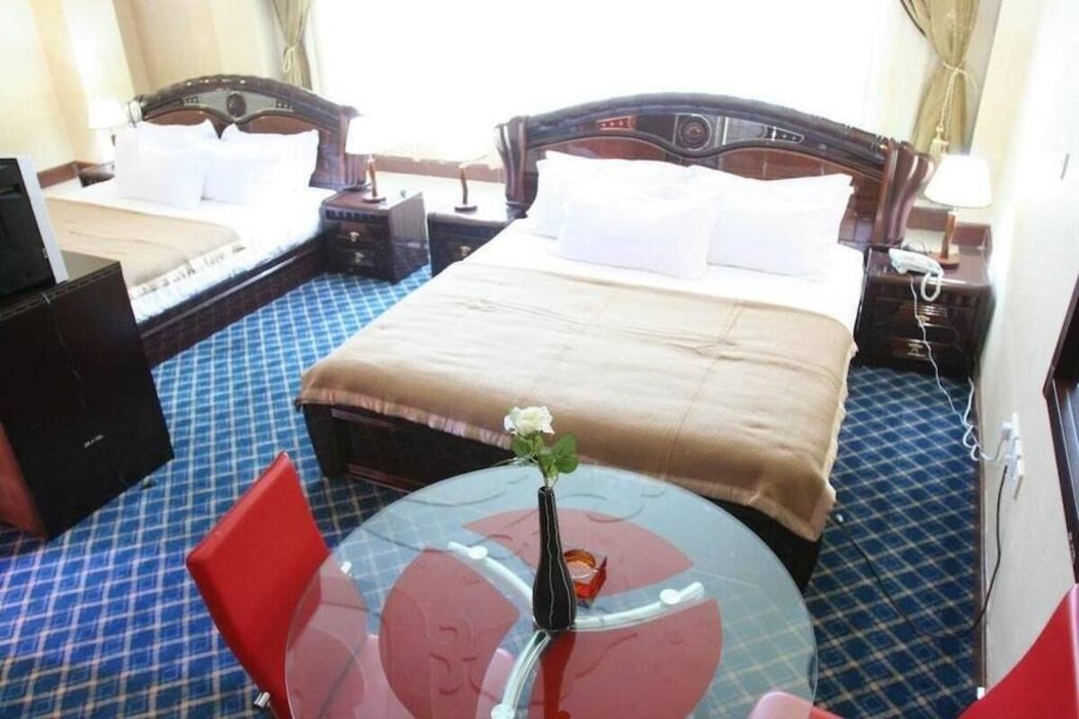 Une chambre d’hôtel avec un lit, deux tables de chevet, une petite table avec un vase et une chaise rouge.