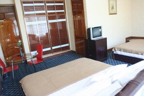 A hotel room with two beds, a TV on a cabinet, a red chair, and a large wooden wardrobe. - JBK Hotel (Kampala)
