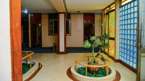A lobby with a central circular planter, a tiled floor, and a glass partition with a grid pattern. - JBK Hotel (Kampala)