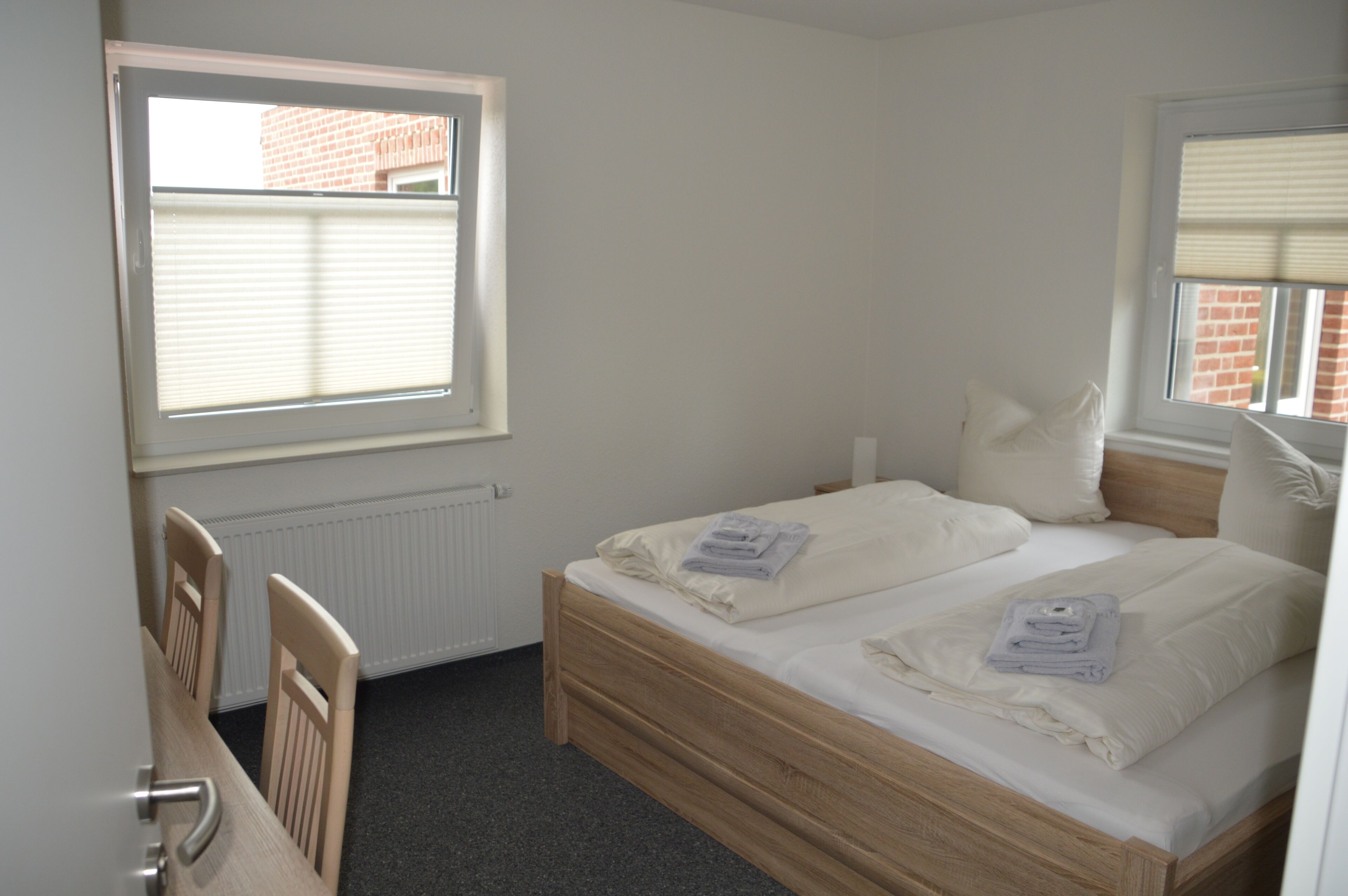 Une chambre à coucher avec un lit en bois, deux oreillers, une table de chevet et une fenêtre avec des stores.
