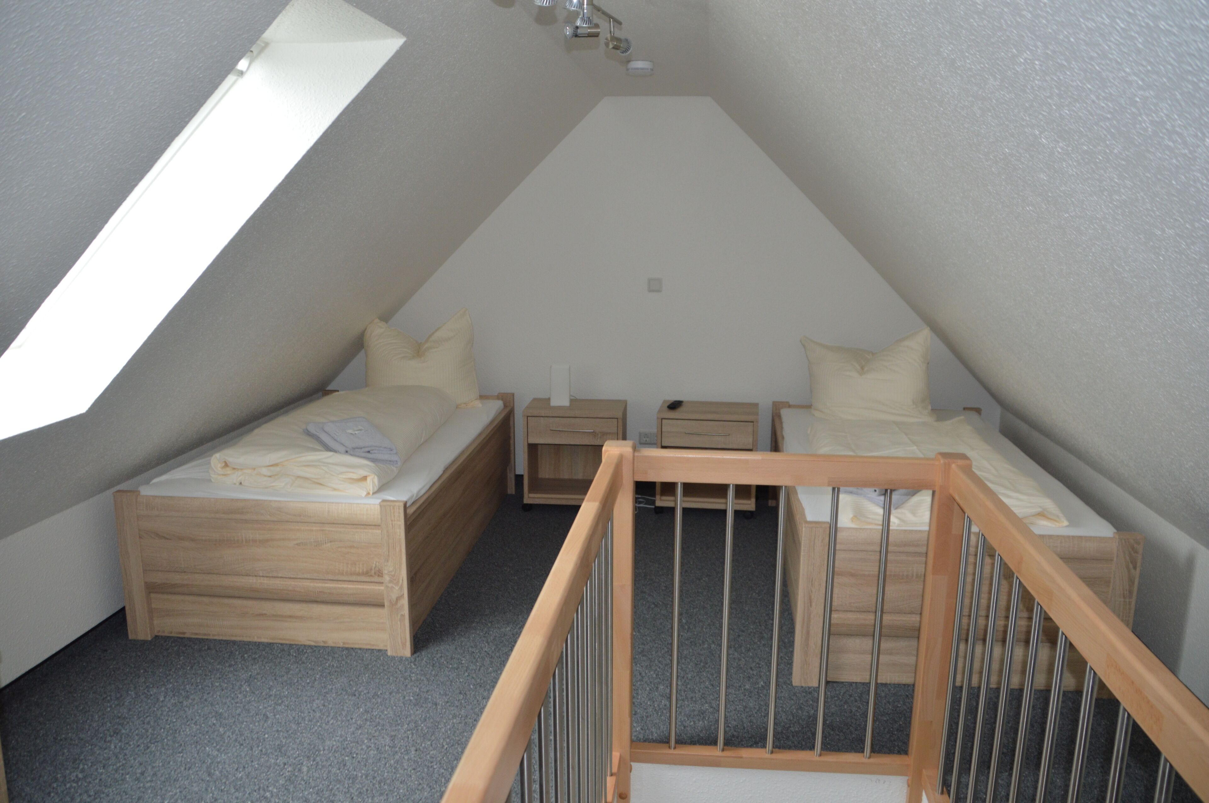 Ein kleines, modernes Schlafzimmer im Dachgeschoss mit zwei Betten, einem Holckrippenbett und einem Oberlicht.