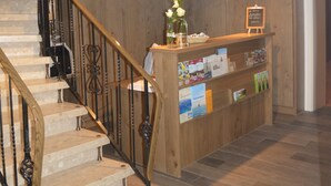 A wooden staircase with a metal railing, a reception desk with brochures, and a ceiling light fixture. - Hotel Zum großen Krug (Wirdum)