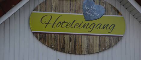 A sign for a hotel named "Hotel Leininga" with a rustic wooden background and a heart-shaped sign above it.