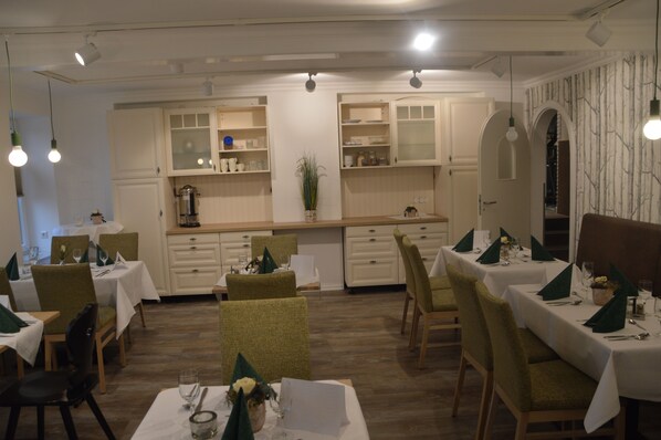 A restaurant with multiple dining tables and chairs, white walls, and wooden flooring. - Hotel Zum großen Krug (Wirdum)