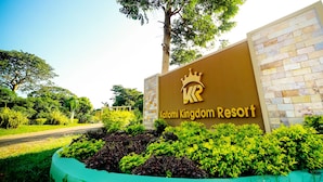 Une enseigne pour le Katomi Kingdom Resort, avec un logo en forme de couronne, entourée d’une végétation luxuriante et d’un mur de pierre.