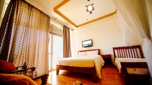 Une chambre d’hôtel avec deux lits, un plancher en bois, un ventilateur de plafond et un téléviseur fixé au mur.