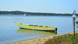 A boat on a calm lake with a distant ship and a lamp post on the shore. - Mirembe Resort Beach Hotel (Bugala Island)