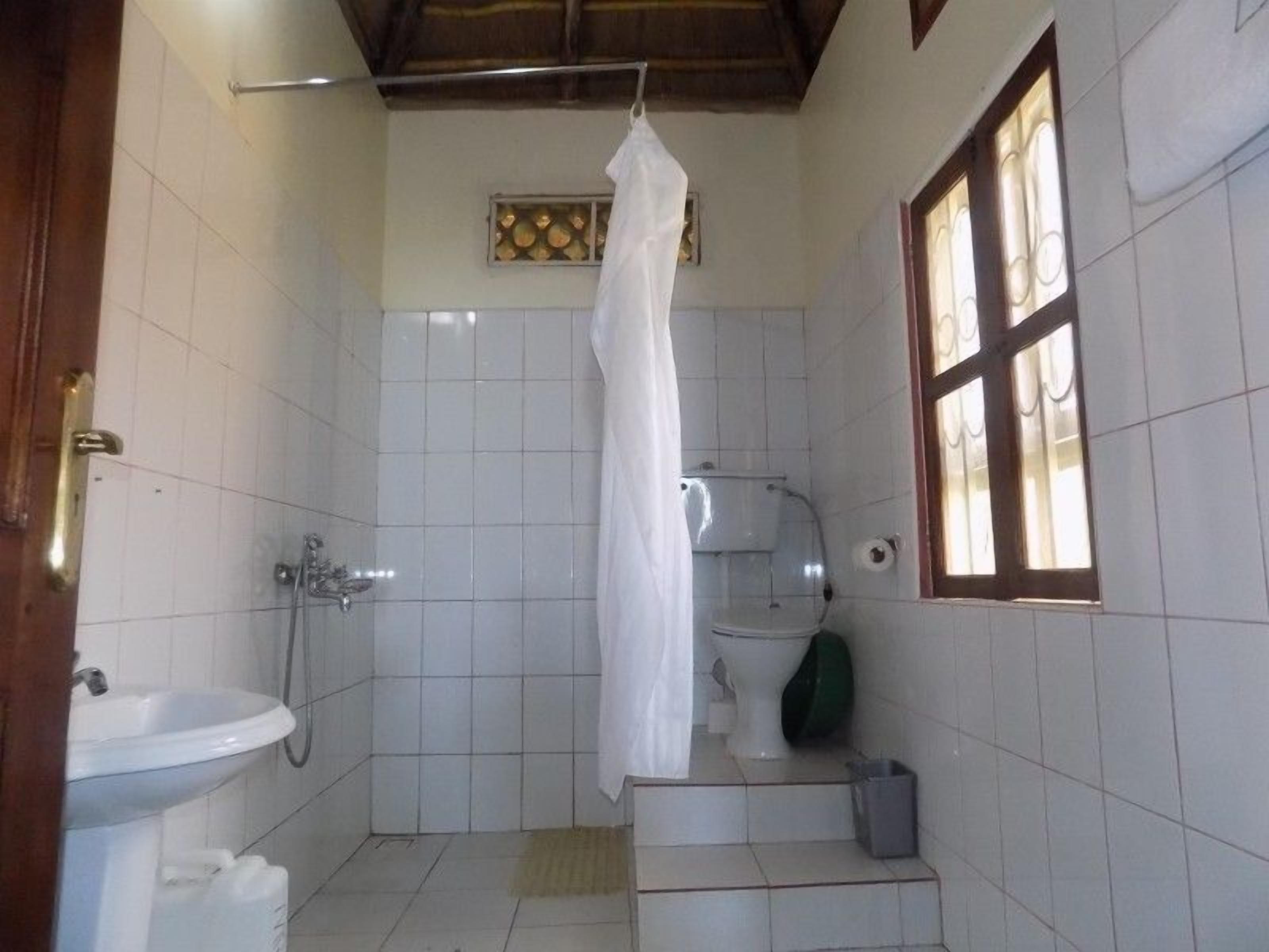 Une petite salle de bain carrelée, équipée d’une douche, de toilettes et d’un lavabo.
