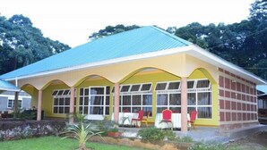 A building with a blue roof, yellow walls, and a covered patio area with red chairs. - Mirembe Resort Beach Hotel (Bugala Island)
