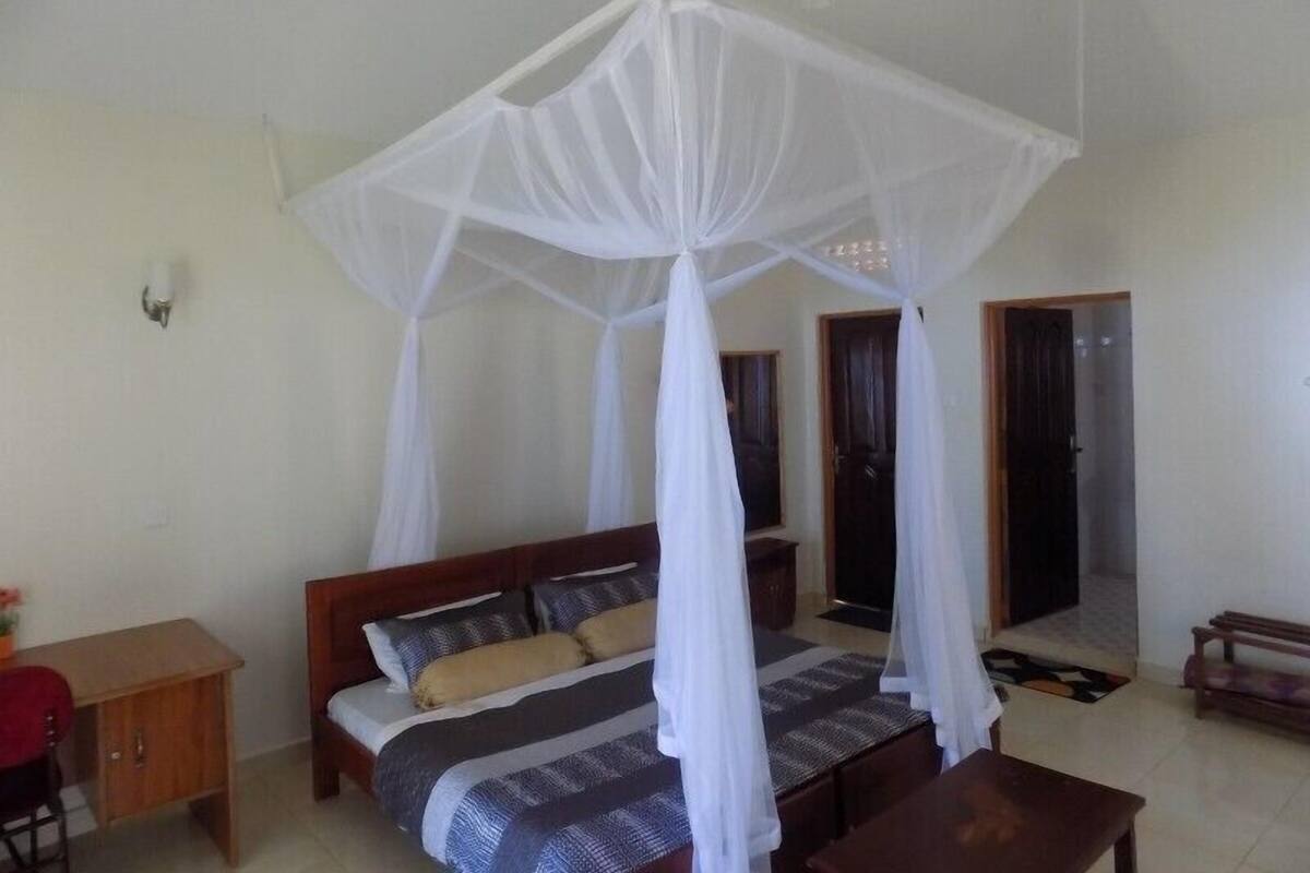 Un dormitorio con una cama bajo un dosel blanco, un escritorio de madera y una mesita.