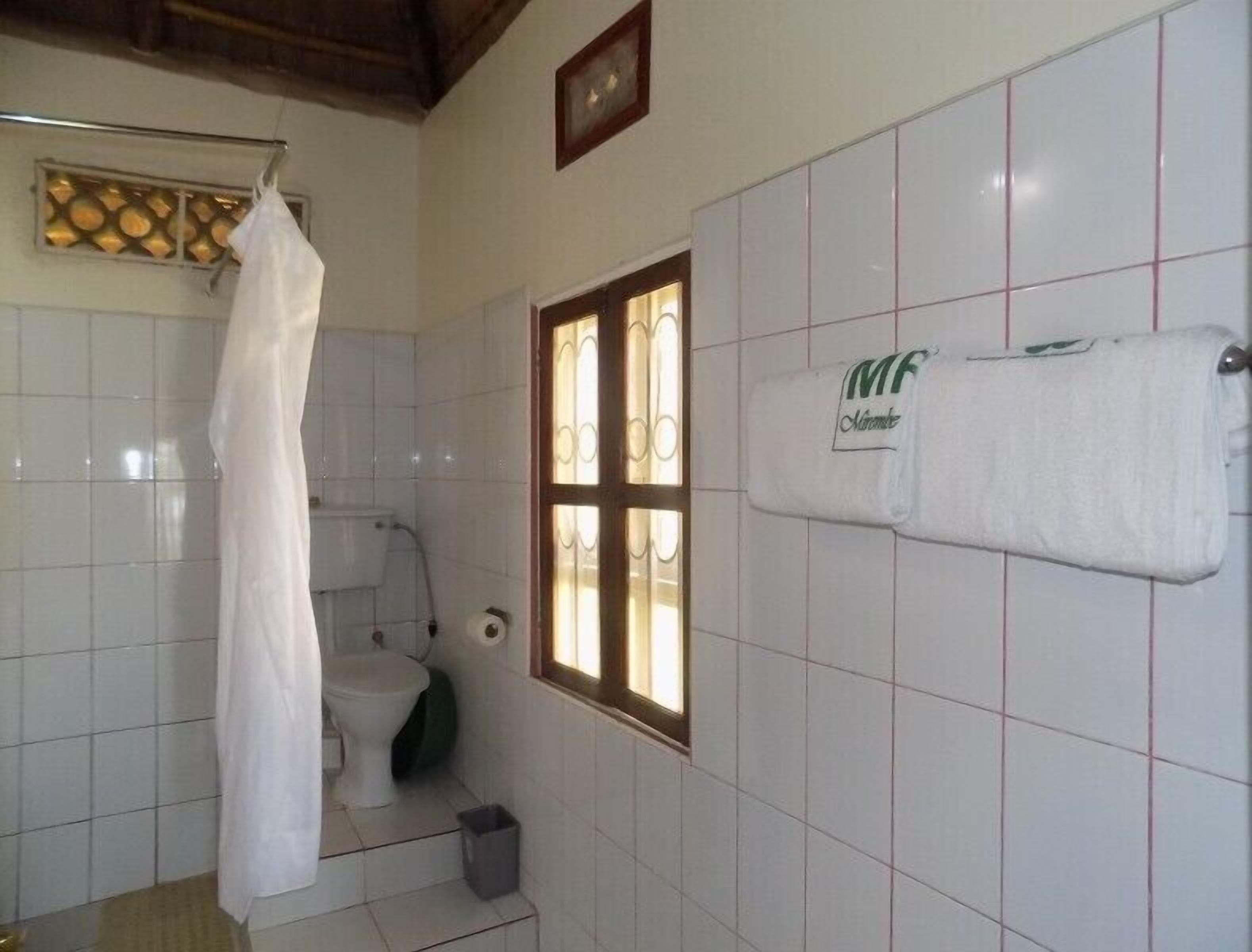 Ein Badezimmer mit weißen Fliesen, einer Toilette, einer Duschvorhang, einem Fenster und einem Handtuch an der Wand.