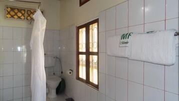 Ein Badezimmer mit weißen Fliesen, einer Toilette, einer Duschvorhang, einem Fenster und einem Handtuch an der Wand.