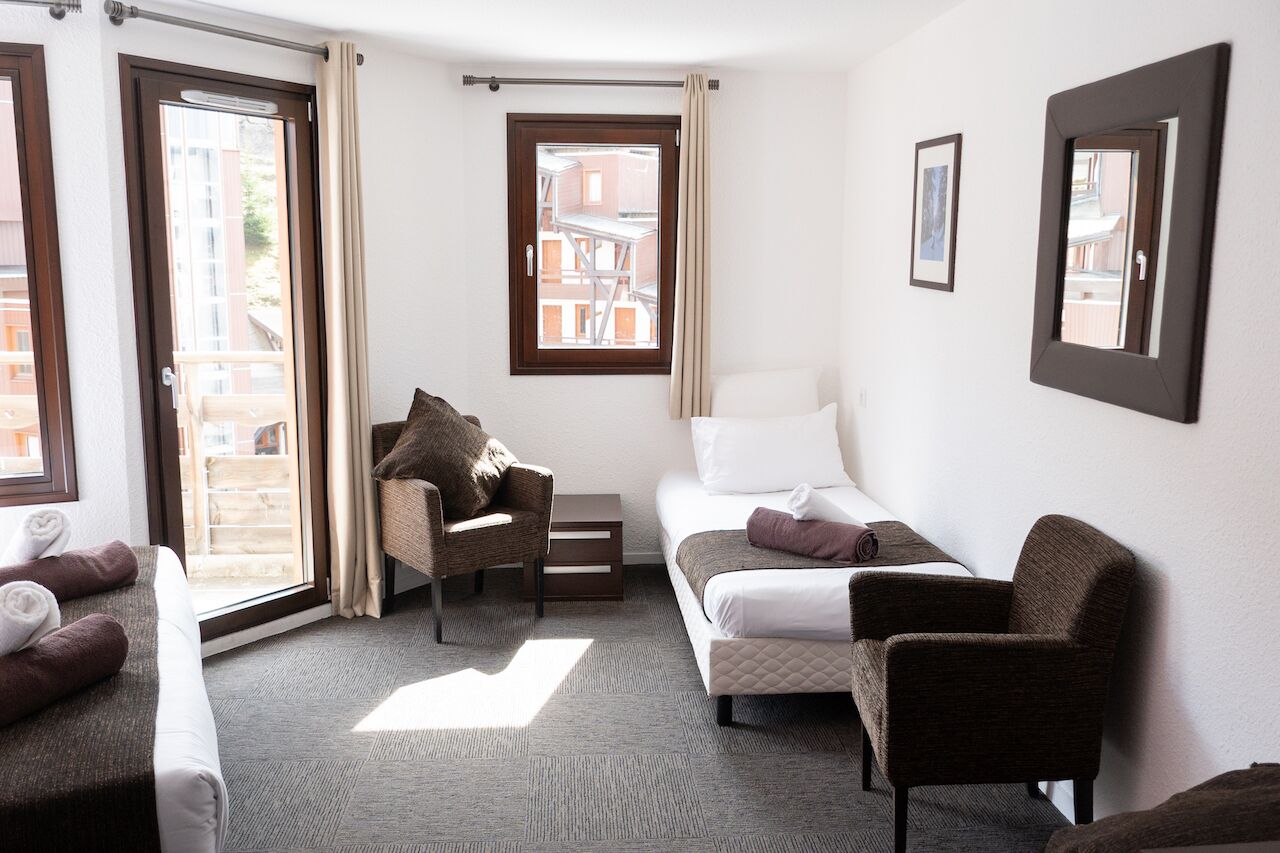 Habitación de hotel con cama, dos sillones, sofá, una mesita y una ventana con cortinas.