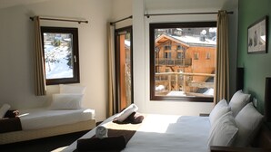 A hotel room with two beds, a large window, and a view of a wooden building outside. - Hôtel Le Montana (Courchevel)