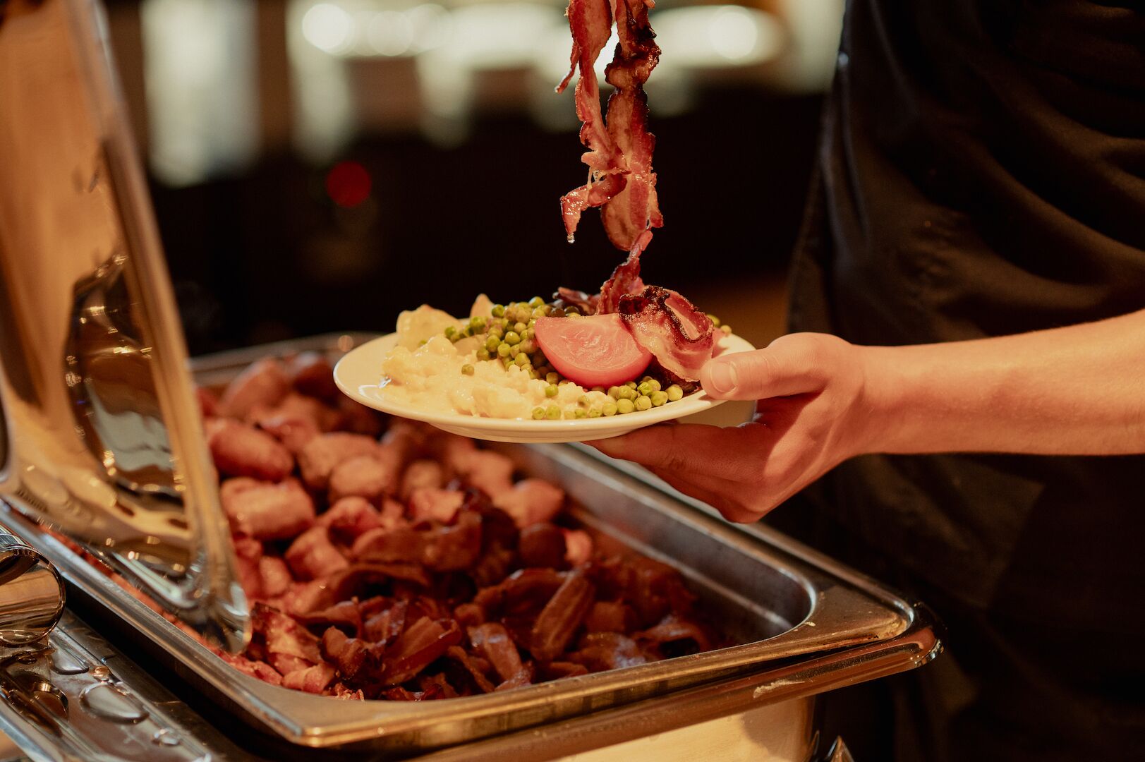 A buffet with various dishes including a plate with peas, a slice of tomato, and bacon.
