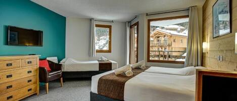 A hotel room with two beds, a wooden dresser, a TV, and large windows with a view of a mountain and buildings.