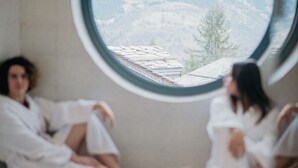 Two individuals in white robes seated in a room with a round window overlooking a mountainous landscape. - Hôtel Le Montana (Courchevel)