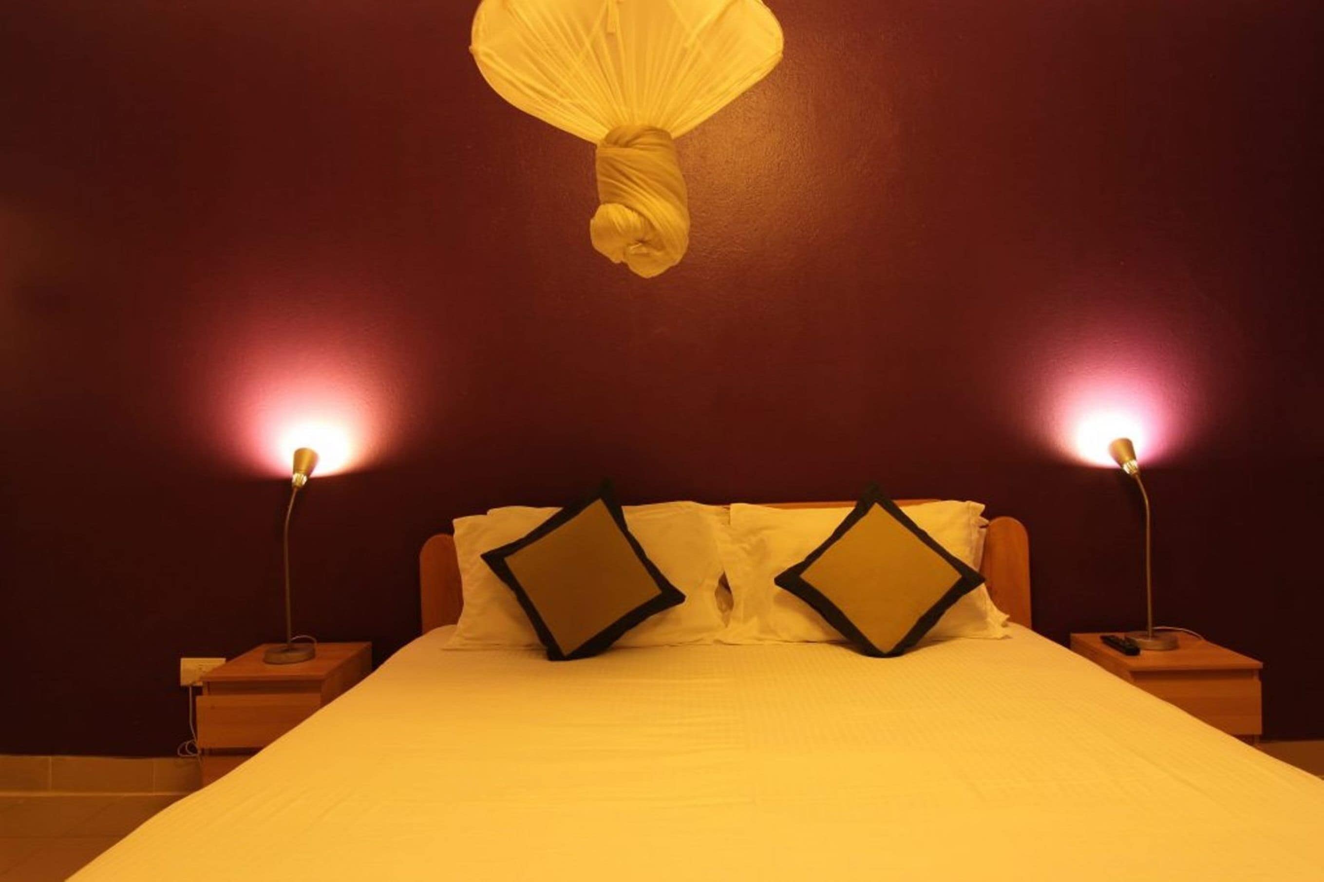 A hotel room with a bed, two bedside lamps, and a hanging light fixture.