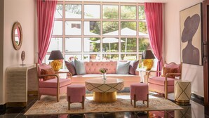 Un salon moderne doté d’une grande fenêtre, de rideaux roses et d’un canapé agrémenté de nombreux coussins.
