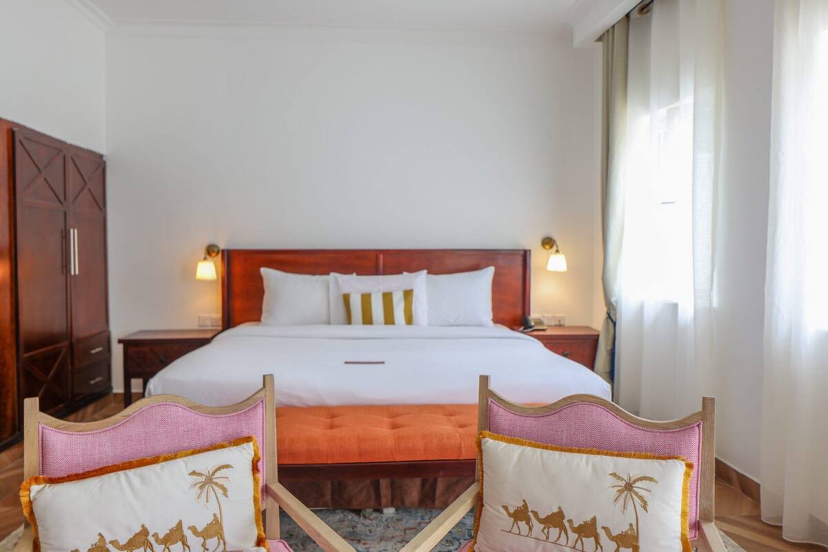 Habitació d'hotel amb un llit gran, dues taules de nit, un armari de fusta i dues cadires amb dibuixos de cavalls dromedaris.