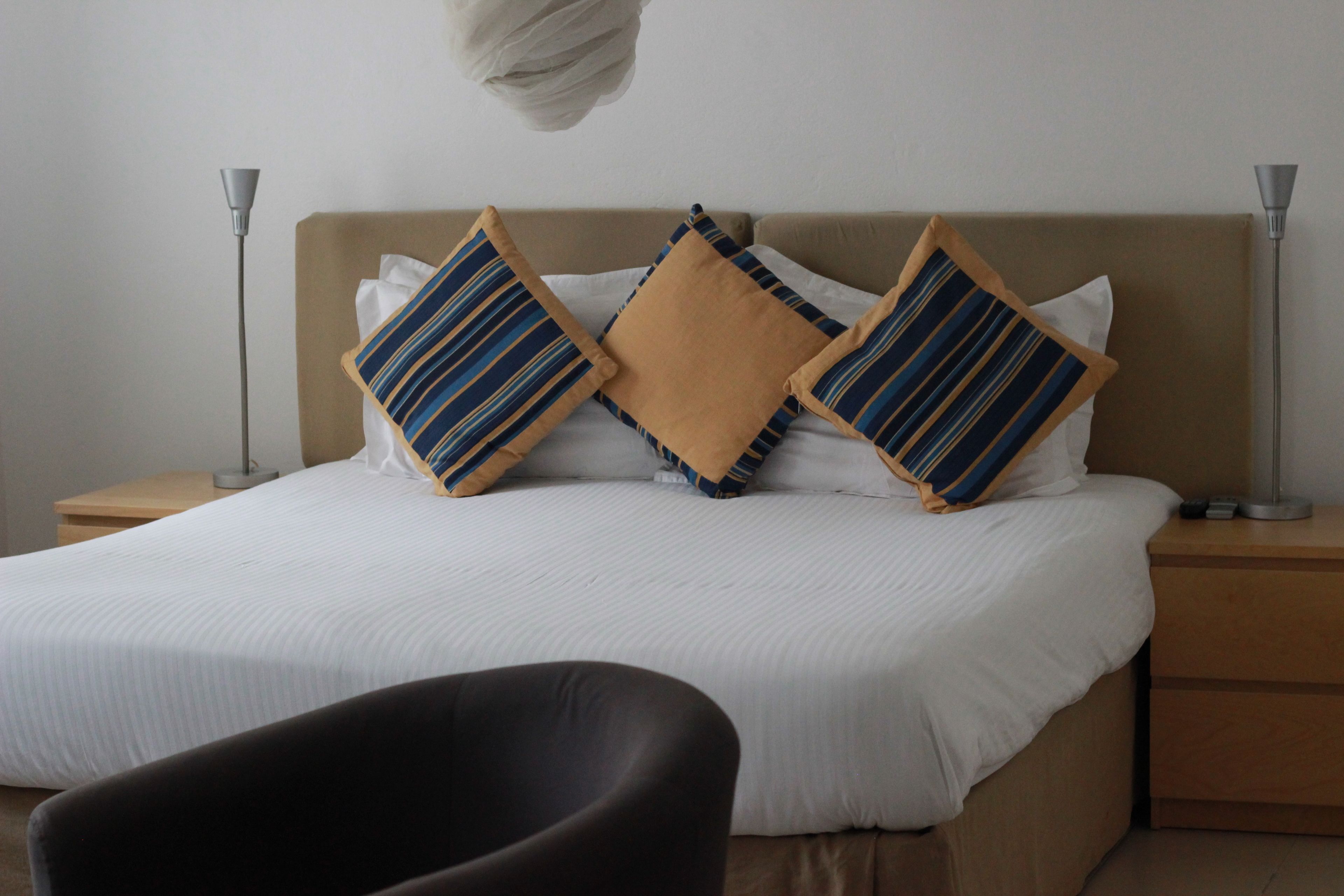 Una cama bien tendida con almohadas a rayas, una lámpara de noche y una silla en una habitación de hotel.