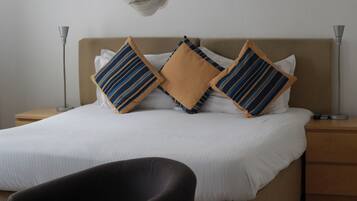 Una cama bien tendida con almohadas a rayas, una lámpara de noche y una silla en una habitación de hotel.