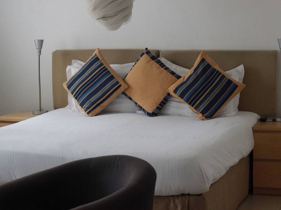 Una cama bien tendida con almohadas a rayas, una lámpara de noche y una silla en una habitación de hotel.