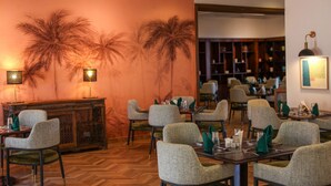 Un restaurant aux murs d’une couleur orange chaleureuse, décoré de fresques représentant des palmiers, et offrant différents types d’aménagements pour s’asseoir.