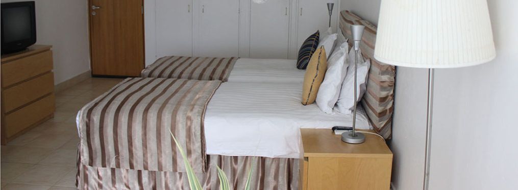 Ein Hotelzimmer mit zwei Betten, einem Holzschrank, einem Fernseher und einer Lampe.