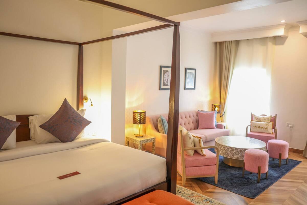 Habitació d'hotel amb un llit amb cortines, una zona de seients amb una taula rodona i cadires, i un sofà separat.