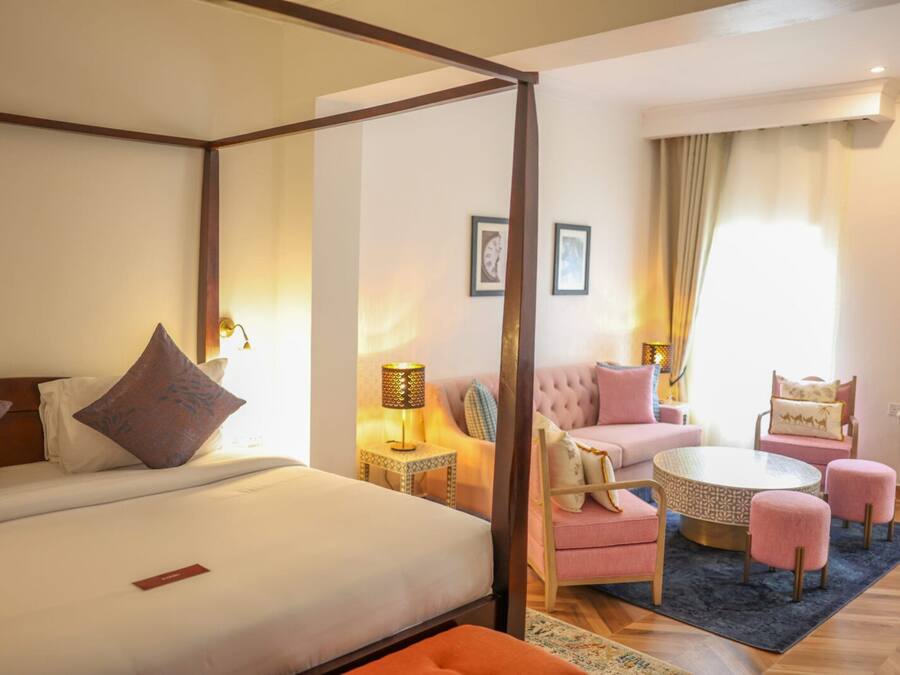 A hotel room with a four-poster bed, a sitting area with a round table and chairs, and a separate sofa.