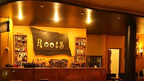 Un espace bar avec une enseigne indiquant « Roots », ainsi que plusieurs tabourets et tables.