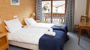 Hotellihuone, jossa on kaksi sänkyä, puinen pääty, pieni pöytä ja näkymä ulkopuolella olevalle parvekkeelle.