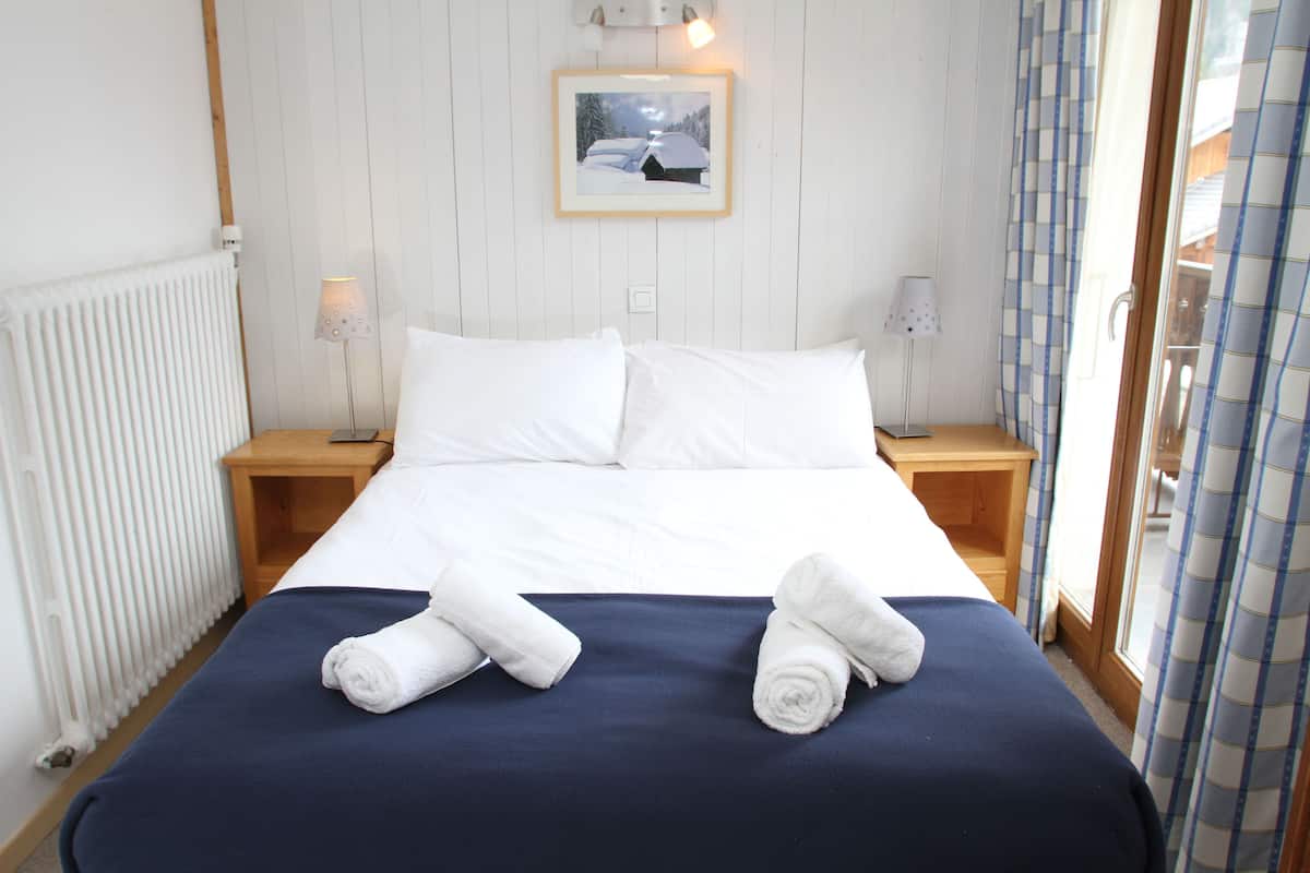 A neatly made bed with white linens and two rolled towels on the bed.