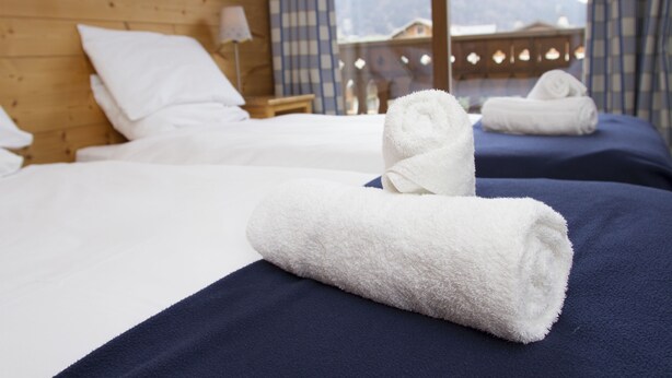 Hotellihuoneessa on kaksi sänkyä, joissa on sininen peitto ja valkoiset tyynyt. Sänkyjen päällä on kaksi rullalle taitettua valkoista pyyhettä.