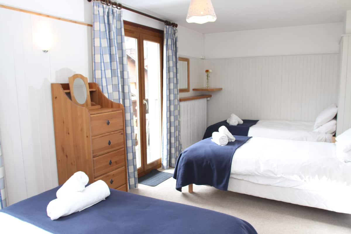 A bedroom with two beds, a wooden dresser, a mirror, and a window with curtains.