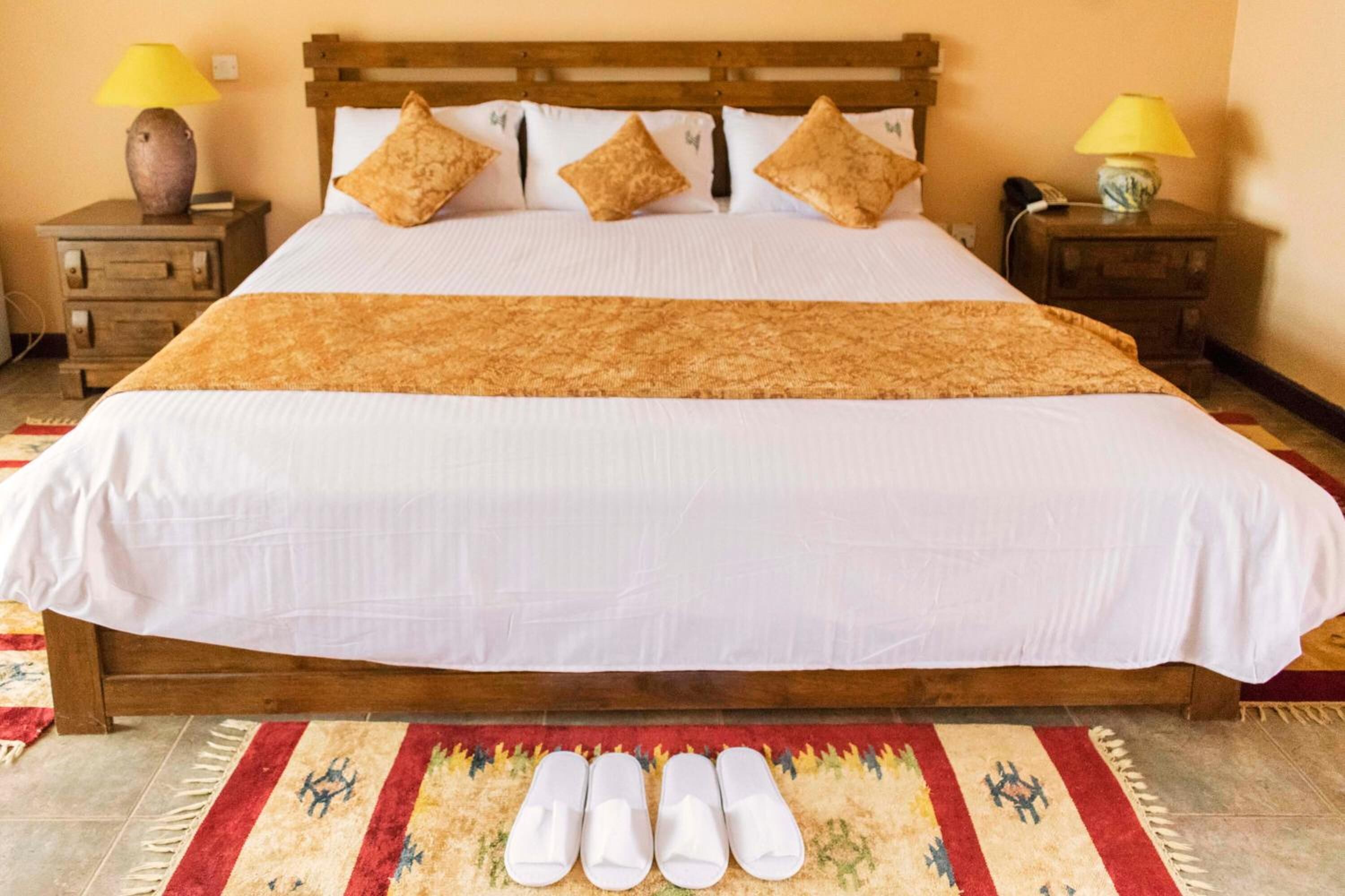 A neatly made bed with a white and brown bedspread, four pillows, and a wooden headboard. There are two bedside tables with lamps and a telephone.