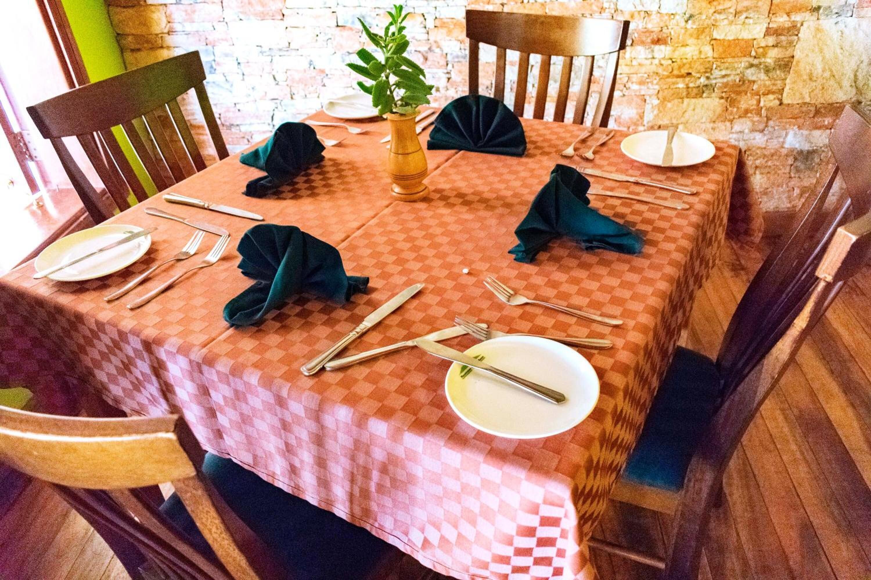 A dining table set with plates, cutlery, and napkins, surrounded by wooden chairs.