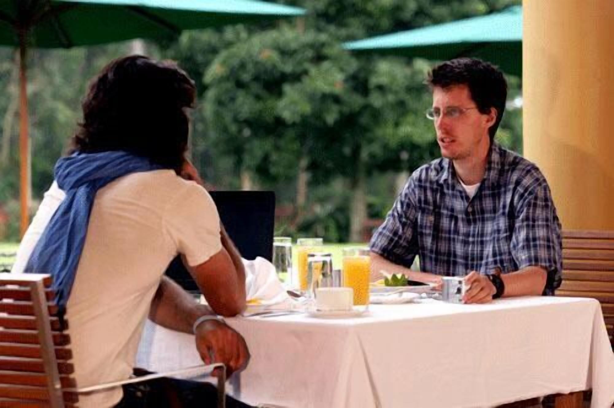 Two people seated at an outdoor table with a white tablecloth, a glass of orange juice, and a cup of coffee.